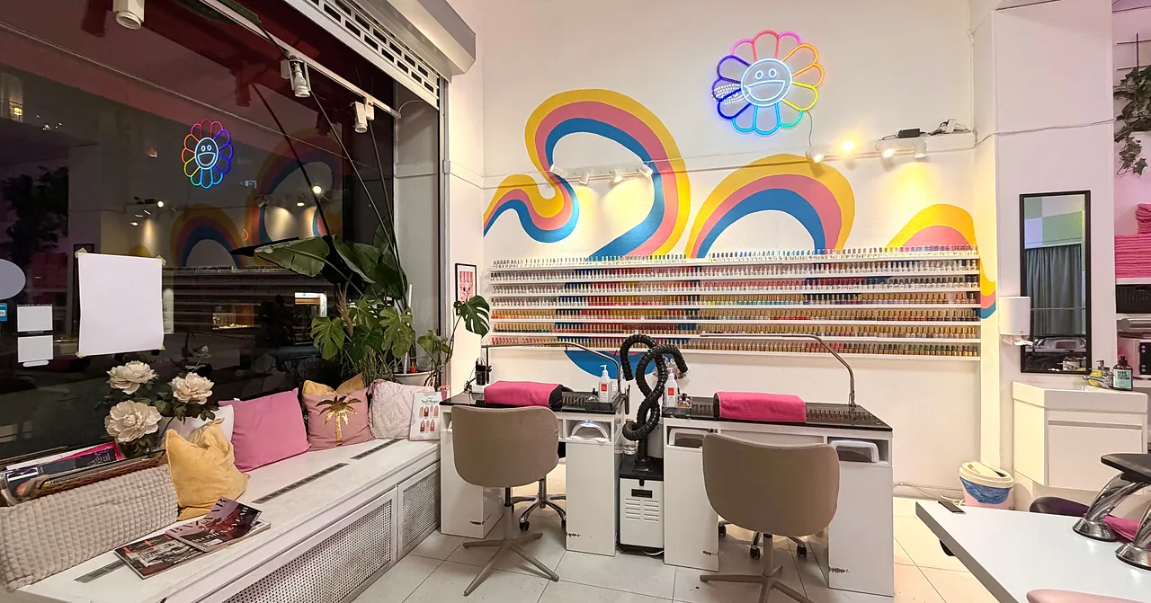 Panoramavy av Polish Nailbars studio i Göteborg med regnbågsmålning, blomsmiley i neon, nagellacksvägg och manikyrstationer.
